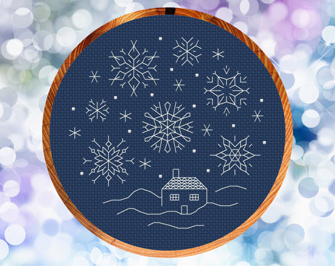 Blackwork Snow Scene cross stitch pattern. Six sided backstitched snowflakes falling on a small cottage. Shown in hoop.