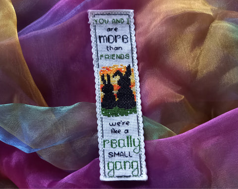 Cross stitched bookmark with silhouette of two bunnies at sunset and the words 'You and I are more than friends  We're like a really small gang'. Bookmark is placed on rainbow fabric.