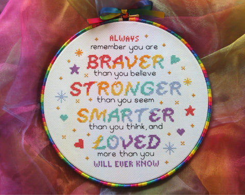 Cross stitch pattern of the quote 'Always remember that you are BRAVER than you believe, STRONGER than you seem, SMARTER than you think, and LOVED more than you will ever know", in rainbow colours. Shown in 10 inch hoop with rainbow ribbon around the hoop.